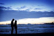 Silhouette of a couple standing on snow-covered tundra.