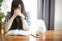 a woman sitting at a table praying over a Bible 