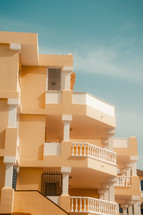 Yellow European apartment block beneath a blue sky, minimal architecture, vacation apartments hotel, colourful building. 