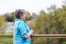 an elderly woman looking over a railing thinking 