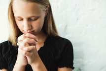 teen girl with head bowed and praying hands 