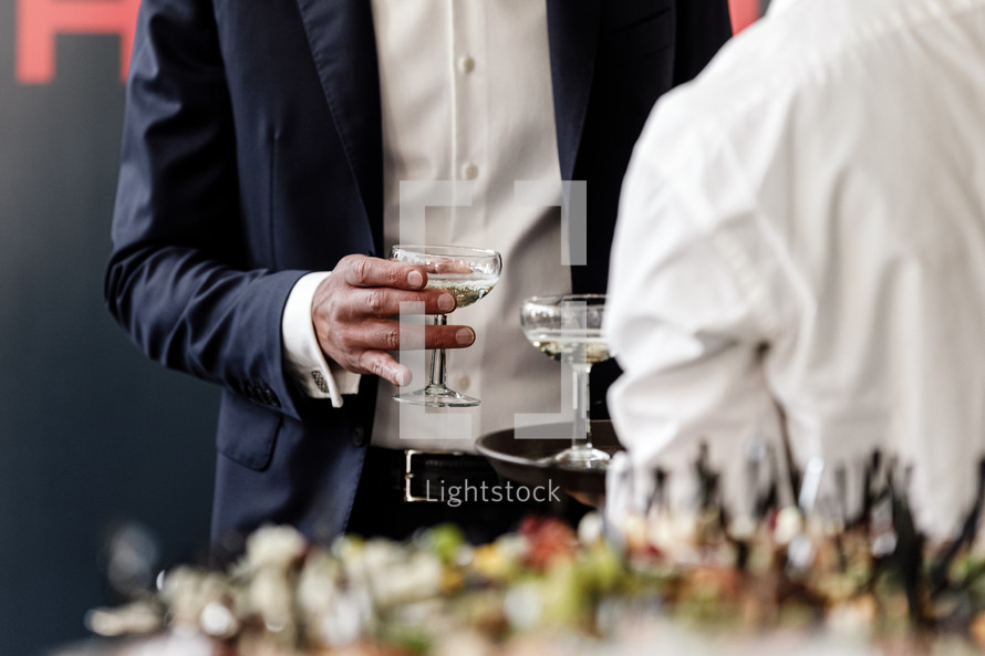 Handsome and successful businessman in stylish suit holding glass of martini on party, corporate party, conference, forums, banquets, closeup. selective focus.