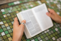 a young woman reading a Bible over a tile table 