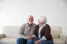 an elderly couple sitting on a couch holding hands 