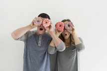a couple holding sprinkled donuts acting silly 