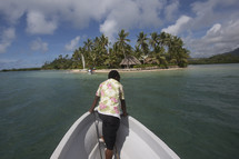 woman on the bow of a boat looking out at tropical water near and island