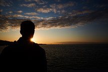 silhouette of a man looking out at water at sunset 