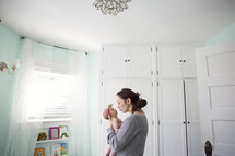 Mother holds infant daughter in white nursery room.