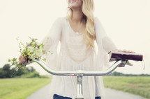 teenage girl riding a bicycle holding a book and flowers.