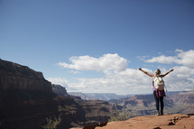 woman standing at the edge of a canyon cliff with raised arms 