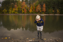 child standing in a pond in rain boots 