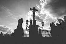 Silhouette of Jesus on the cross with statues in a courtyard.