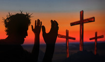 Jesus with crown of thorns praying with hands raised and three crosses in the background