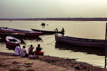 fishing boats and people sitting along a shore 