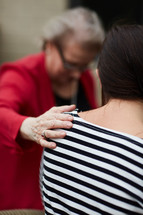 elderly woman praying over a young woman 