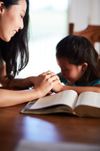 mother and daughter reading the Bible and holding hands together at the kitchen table 