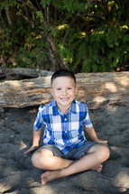 a boy smiling sitting in the sand 