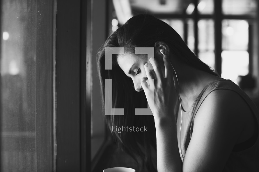 a young woman in front of a window listening to earbuds 