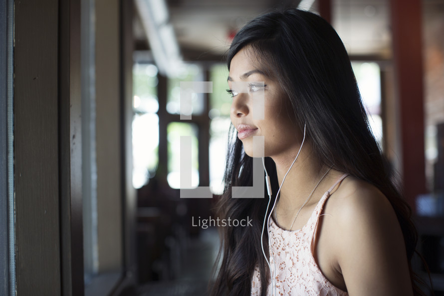 a young woman listening to earbuds in front of a window in a coffee shop 