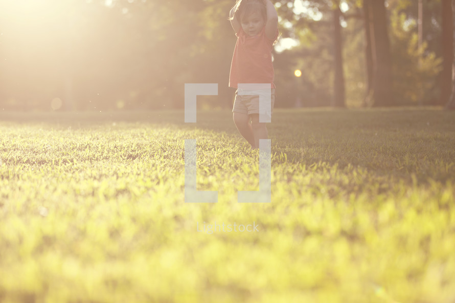 toddler girl walking in the grass at sunset.