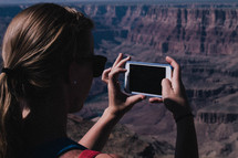 a woman taking pictures of a canyon with her cellphone 