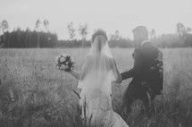 a bride and groom walking through a field of tall grasses 