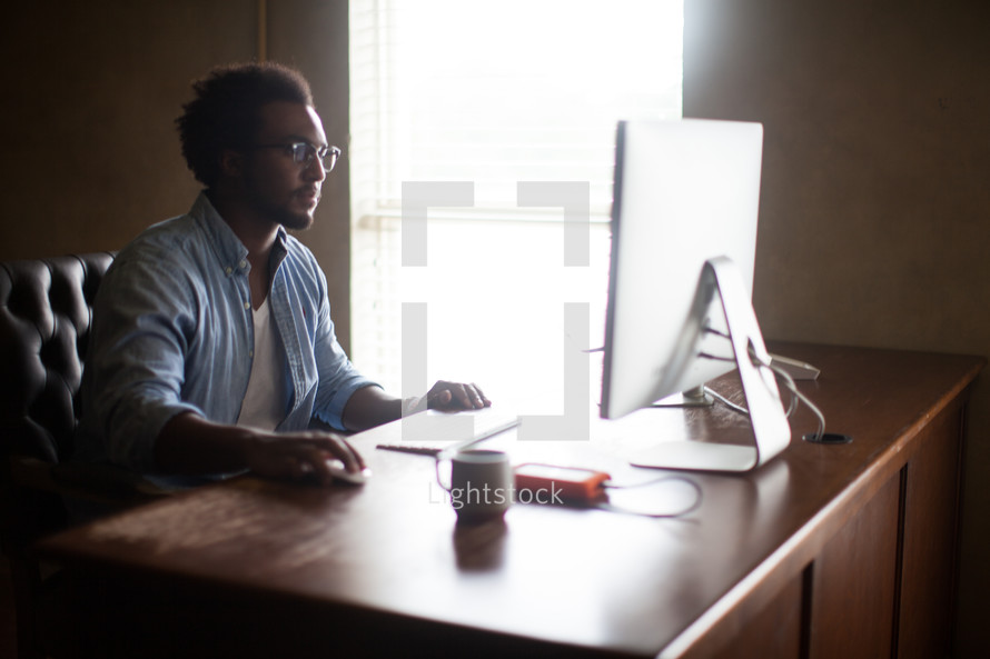 An African American man sitting at a desk typing on a computer 
