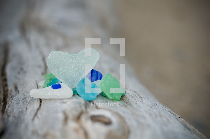 Blue, white and green colored stones,one a heart shape, laying on a tree trunk