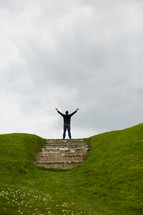 a man with arms raised standing at the top of a hill 
