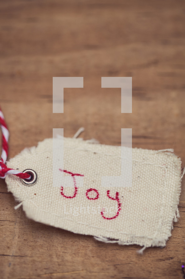 A Christmas gift tag with "Joy" written on it, on a wood grain background.