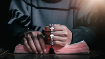 a man holding a beaded bracelet and praying 