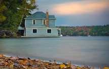 A cottage sits on a lake. Colorful trees highlight the background. (3o second exposure)
