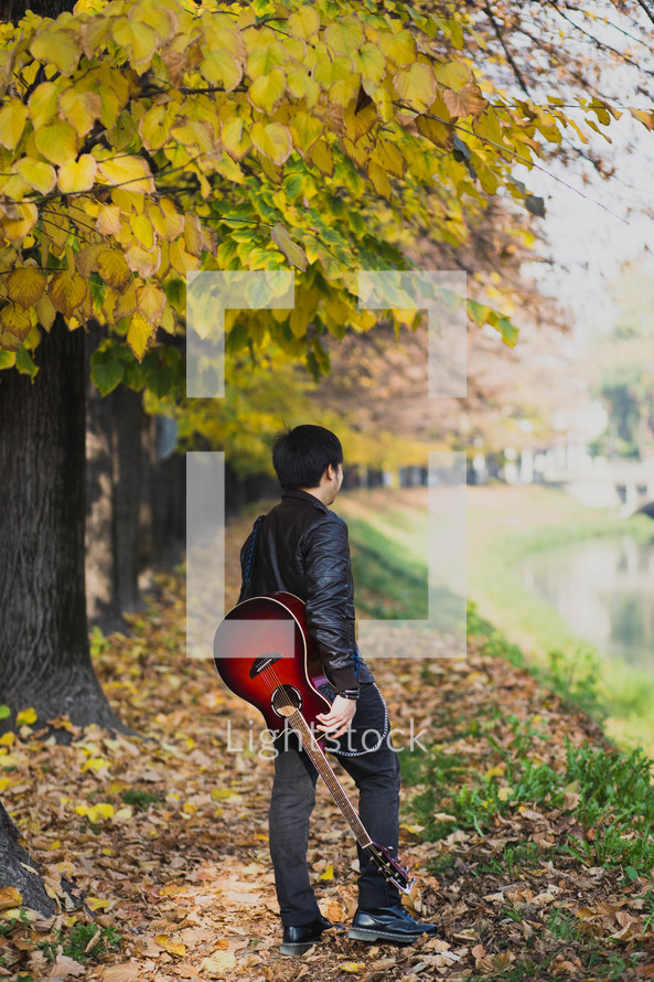 a teen boy walking with a guitar outdoors 
