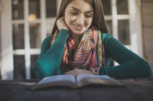 A young woman smiling and reading the Bible