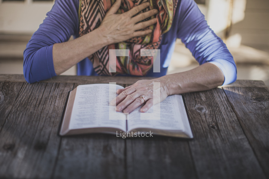 A woman reading the Bible with her hand over her heart