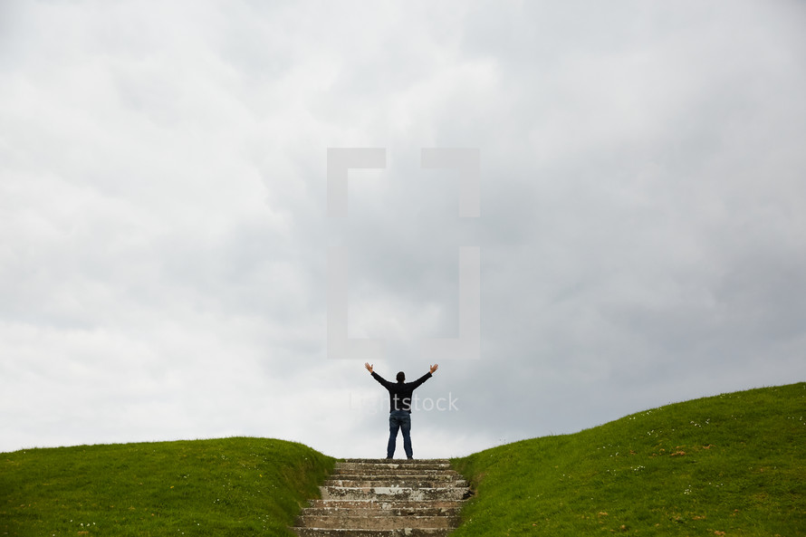 a man standing at the top of a hill with arms raised 