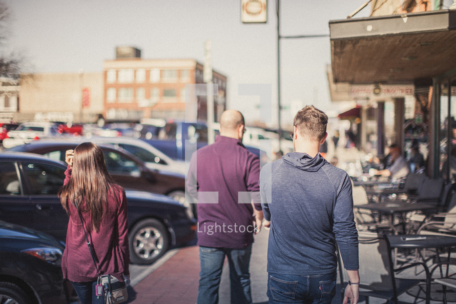 Young people walking down the sidewalk in front of a cafe