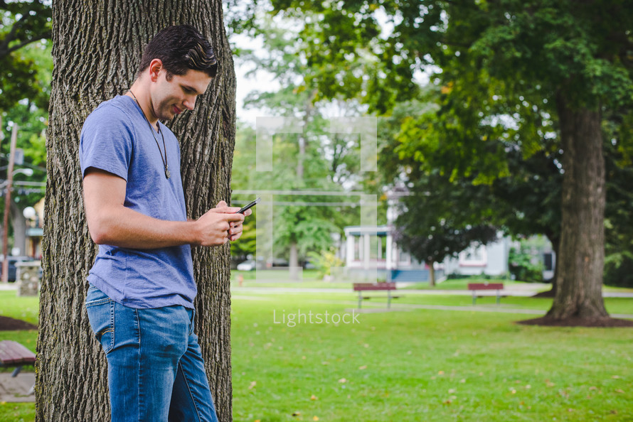man standing beside a tree texting 