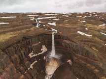 aerial view over a waterfall flowing over brown cliffs 