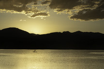 A Silhouette Paddleboarder with their dog on a mountain lake at sunset located in Loveland Colorado