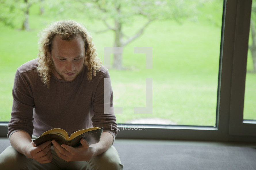a man sitting in a window reading a Bible 