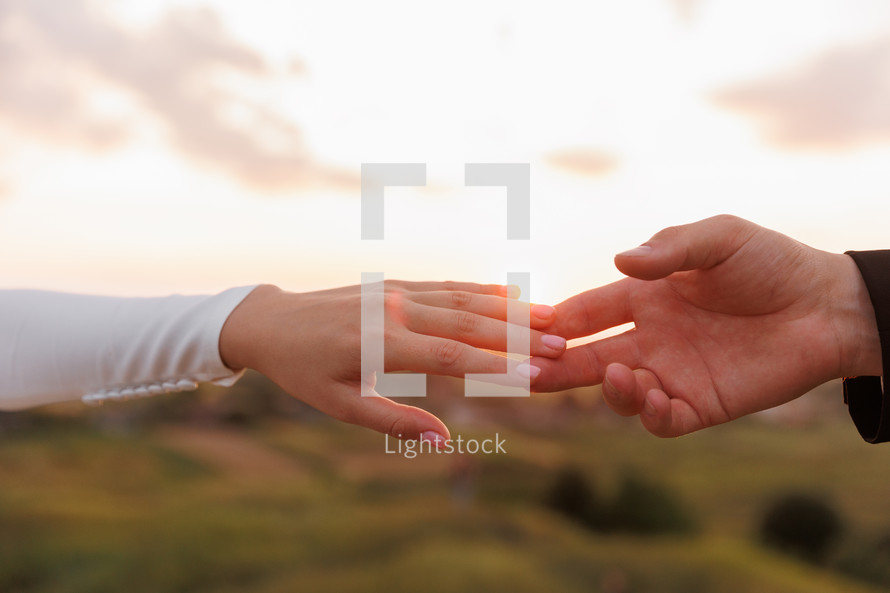 Hand of man and woman reaching and touching to each other with love on nature sunset sky background. Valentines day. Concept of human relation, community, togetherness, teamwork, love, symbolism