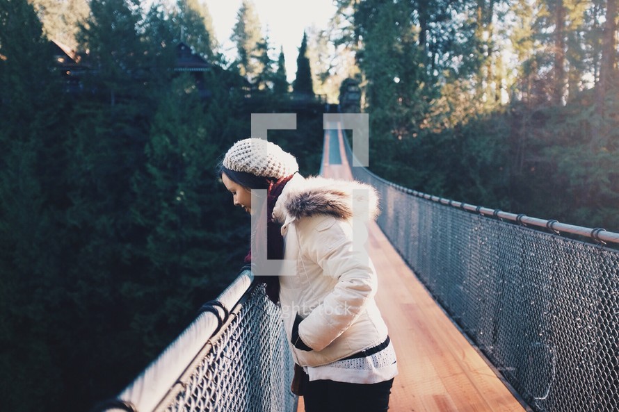 a woman walking across a swinging bridge and looking down 