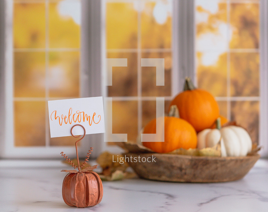 Orange and white pumpkins with a welcome sign in front of autumn window