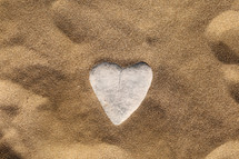 Stone in the form of a heart on sand. Sea sand background, wallpaper. valentines day, wedding, honeymoon or love greeting card concept.
