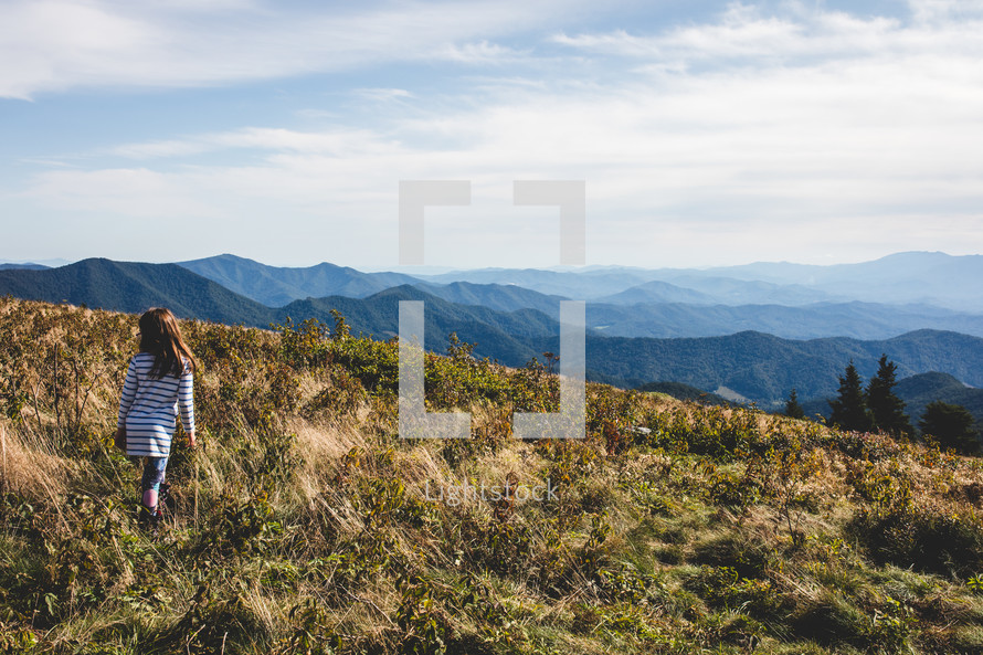 a girl walking through a field on a mountaintop 