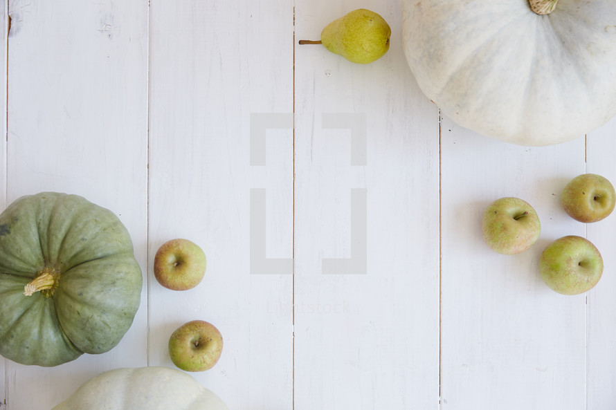 pumpkins, apples, and pears on white wood boards 
