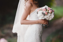 The bride in an elegant wedding dress holds a beautiful bouquet of different flowers and green leaves. Wedding theme.