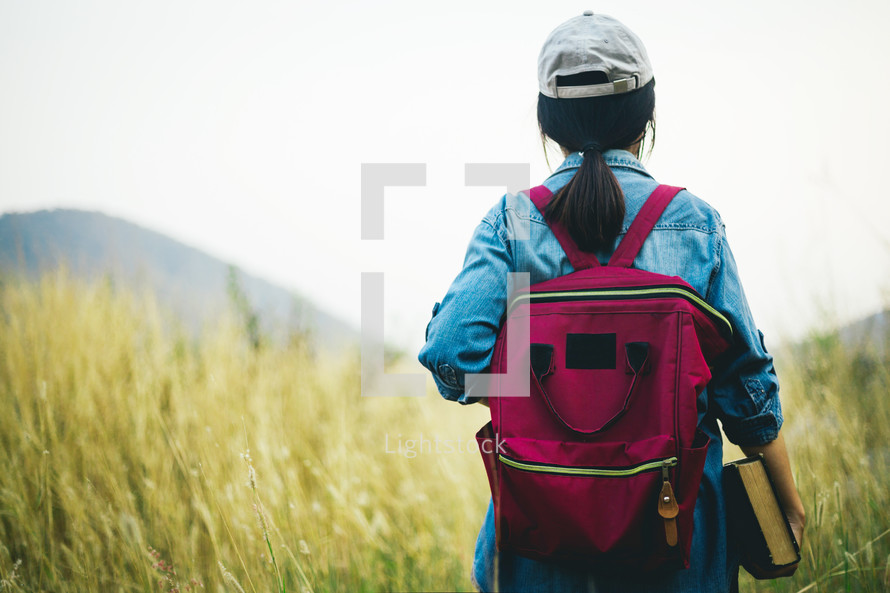 a girl carrying a Bible walking through a field 