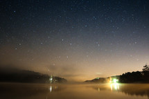A starry night sky over a foggy lake 